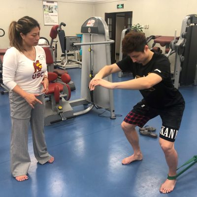 Dr. Lilian Chen working with male badminton athlete on hip alignment using resistance band around knees
